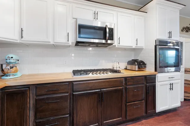 a kitchen with stainless steel appliances kitchen island granite countertop a sink dishwasher a stove top oven a refrigerator with white cabinets and wooden floor