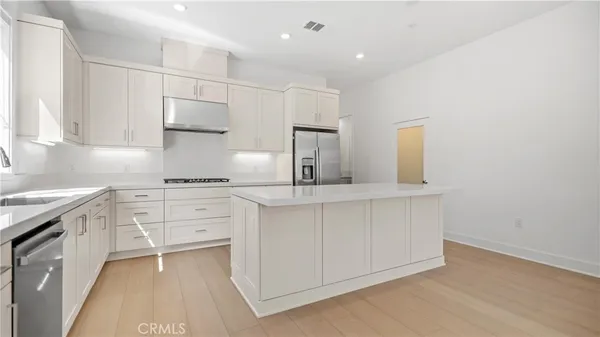 a large white kitchen with stainless steel appliances granite countertop a large counter top and a stove with wooden floor