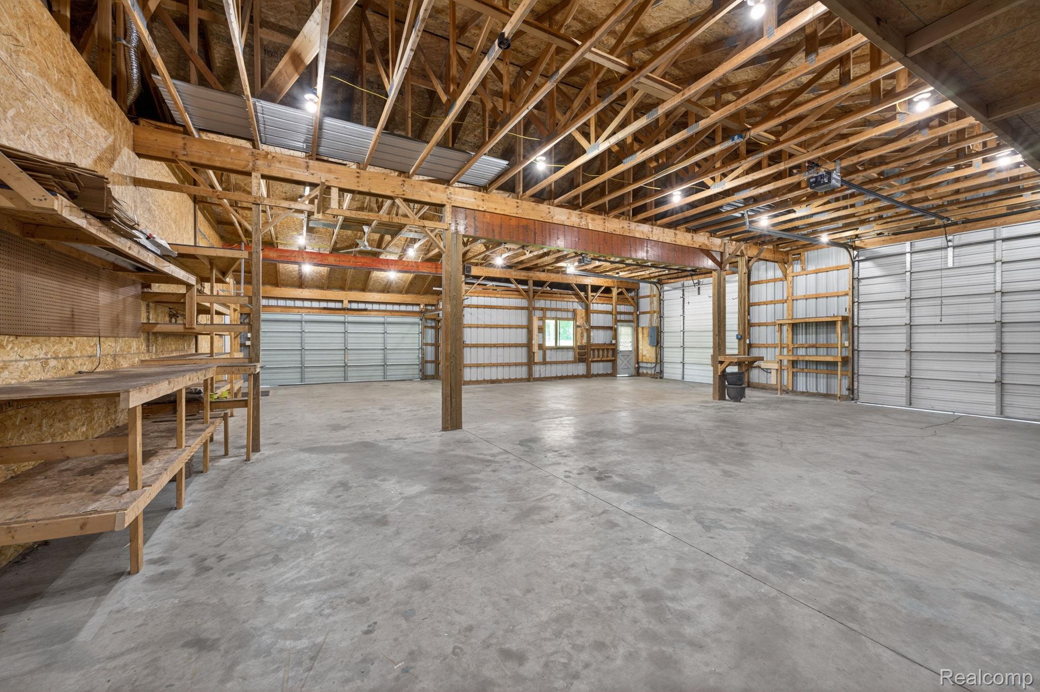 9353 Hill Road Swartz Creek, MI 48473 - Photo 78 of 98 Spacious interior building featuring a concrete floor, exposed wood beam ceiling, corrugated metal walls, multiple roll-up garage doors, and built-in shelving and workbenches