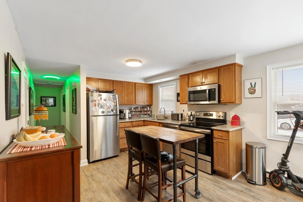 299 Asbury Street Hamilton, MA 01982 - Photo 4 of 37 a kitchen with stainless steel appliances a refrigerator a stove a microwave a dining table and chairs with wooden floor