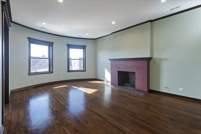 an empty room with wooden floor fireplace and windows