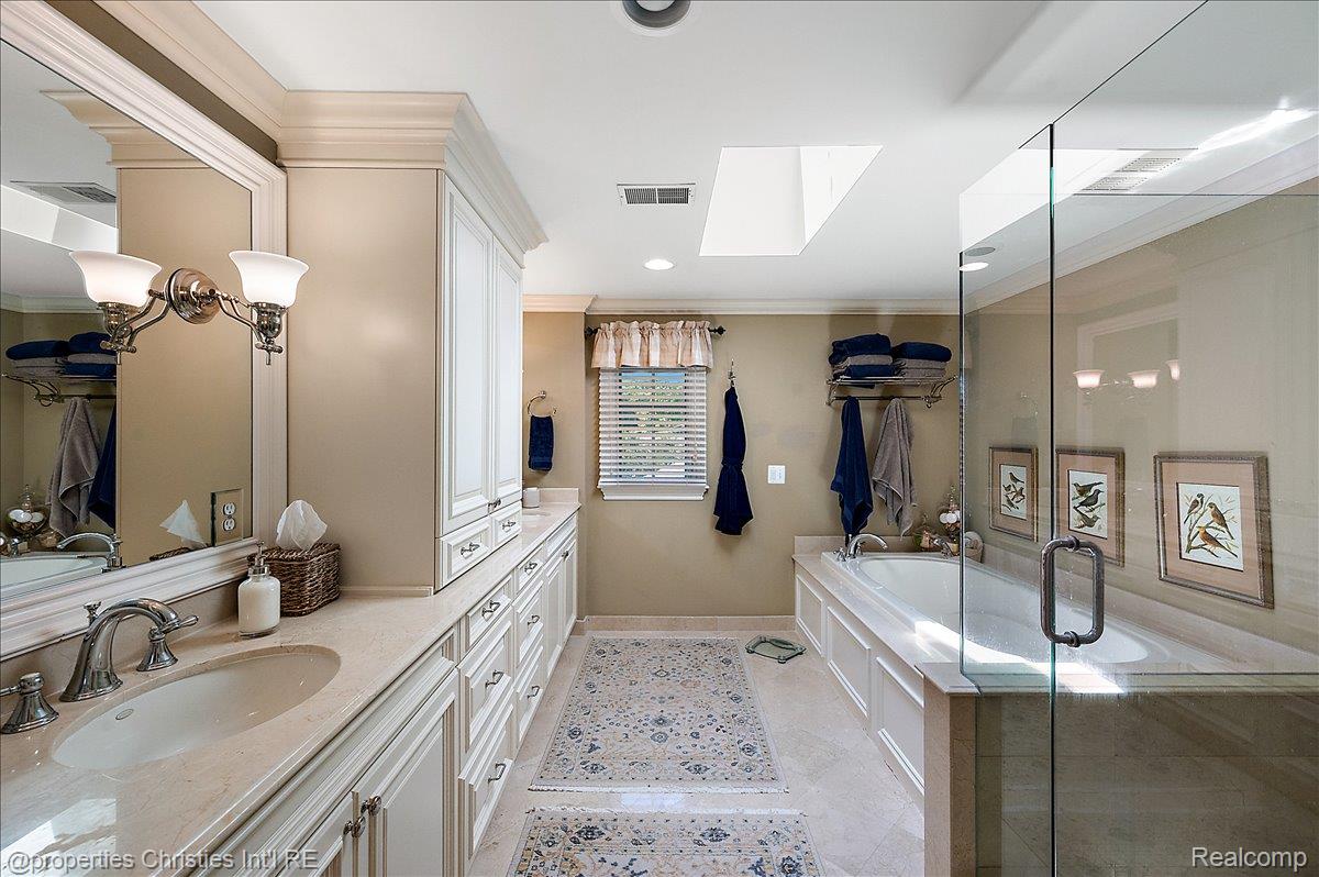 135 Clifton Road Bloomfield Hills, MI 48301 - Photo 39 of 77 Spacious bathroom featuring a dual vanity with a light-toned countertop, extensive white cabinetry, a built-in soaking tub, a frameless glass shower enclosure, and a skylight