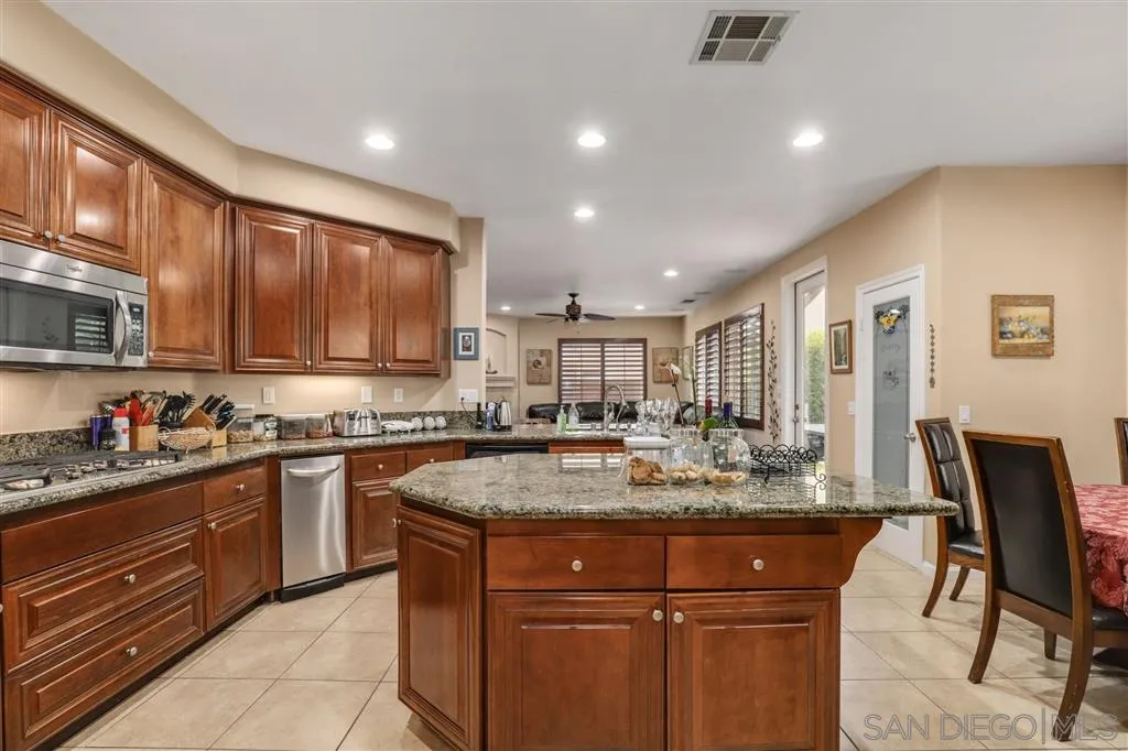 8403 Watson Ranch Road San Diego, CA 92129 - Photo 9 of 25 a kitchen with stainless steel appliances granite countertop a stove top oven a sink dishwasher a dining table and chairs with wooden cabinets