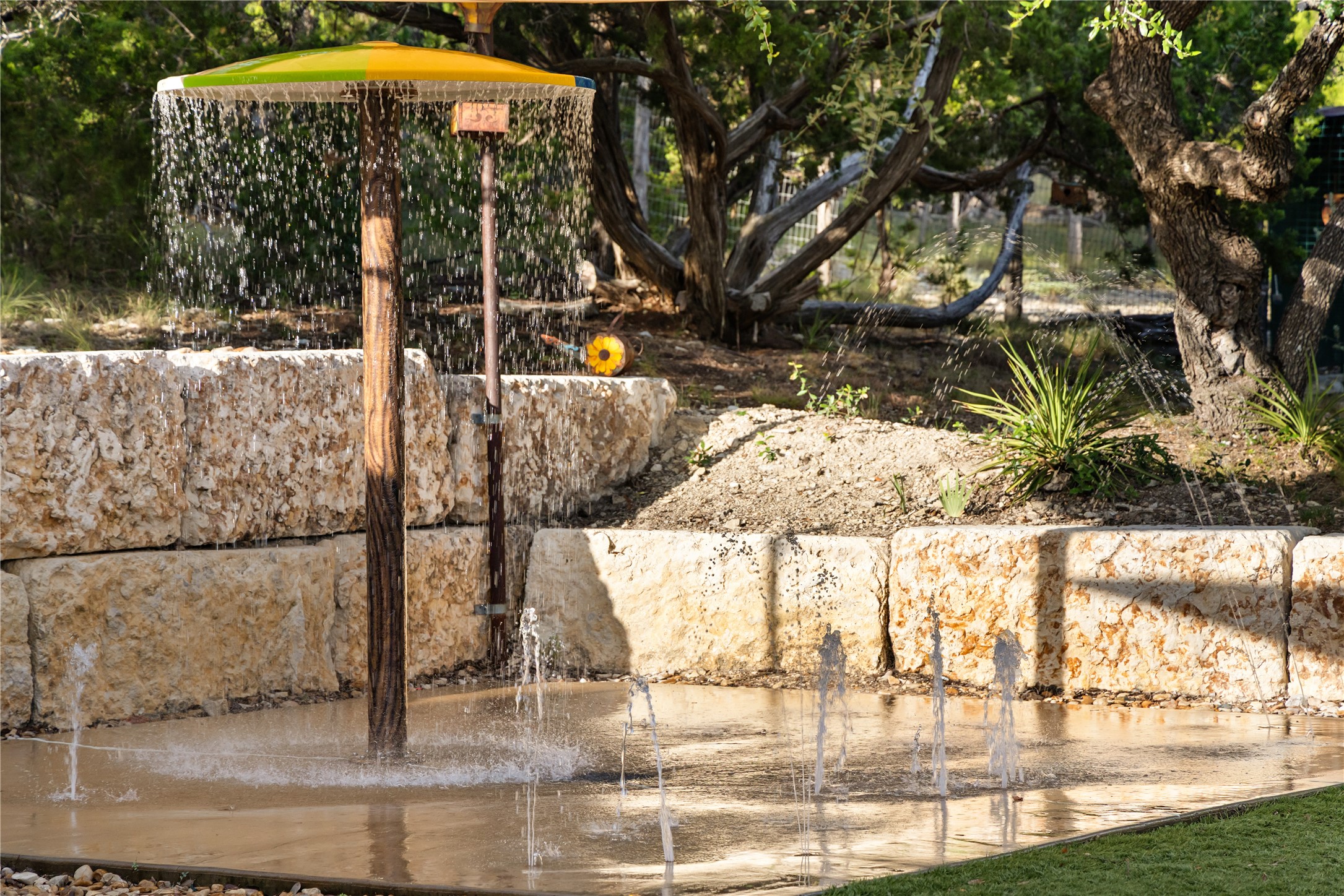 1017 Westland Ridge Road Dripping Springs, TX 78620 - Photo 3 of 40 A private splash pad water feature is framed by natural stone retaining walls and mature trees.