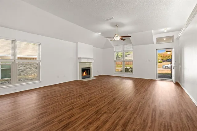 an empty room with wooden floor fireplace and windows