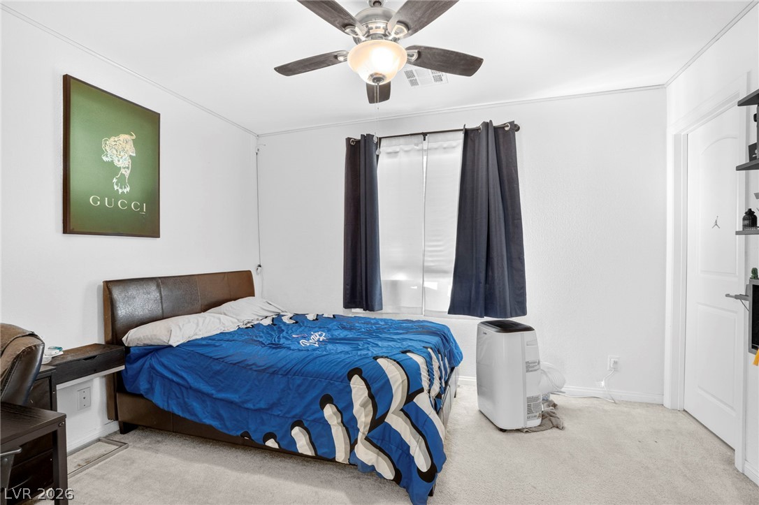 6281 Angora Peak Lane Las Vegas, NV 89115 - Photo 25 of 34 A well-lit bedroom features a window with dark curtains, a contemporary ceiling fan, and light-toned carpeting.