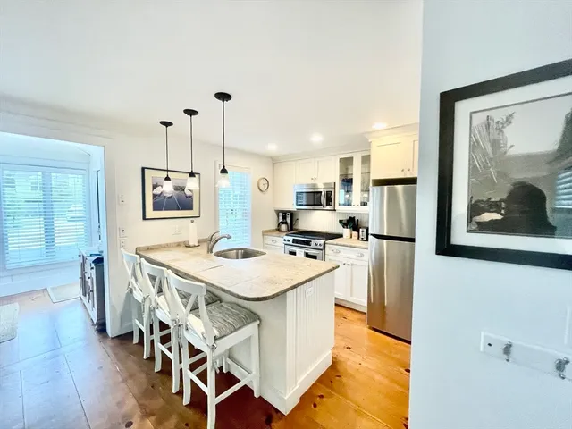 a open kitchen with stainless steel appliances kitchen island a stove a refrigerator a dining table and chairs with wooden floor