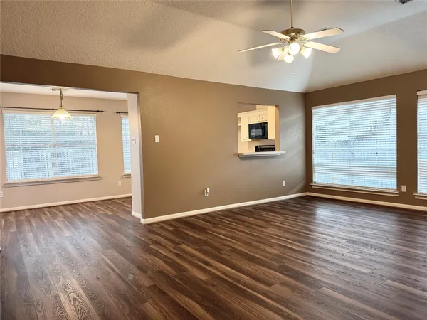 an empty room with wooden floor chandelier fan and windows