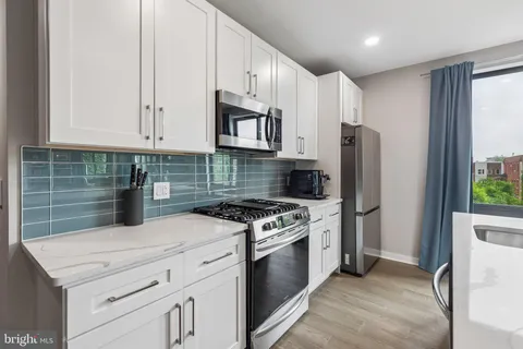 a kitchen with stainless steel appliances kitchen island granite countertop a stove top oven a sink a refrigerator white cabinets and wooden floor
