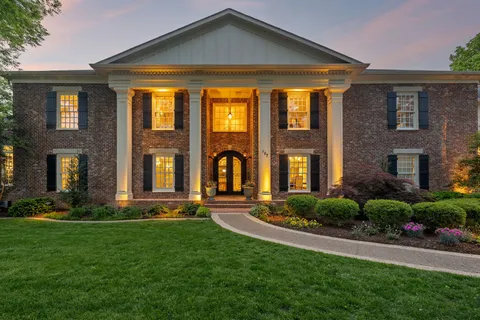 a view of a white house with a big yard and potted plants and large trees