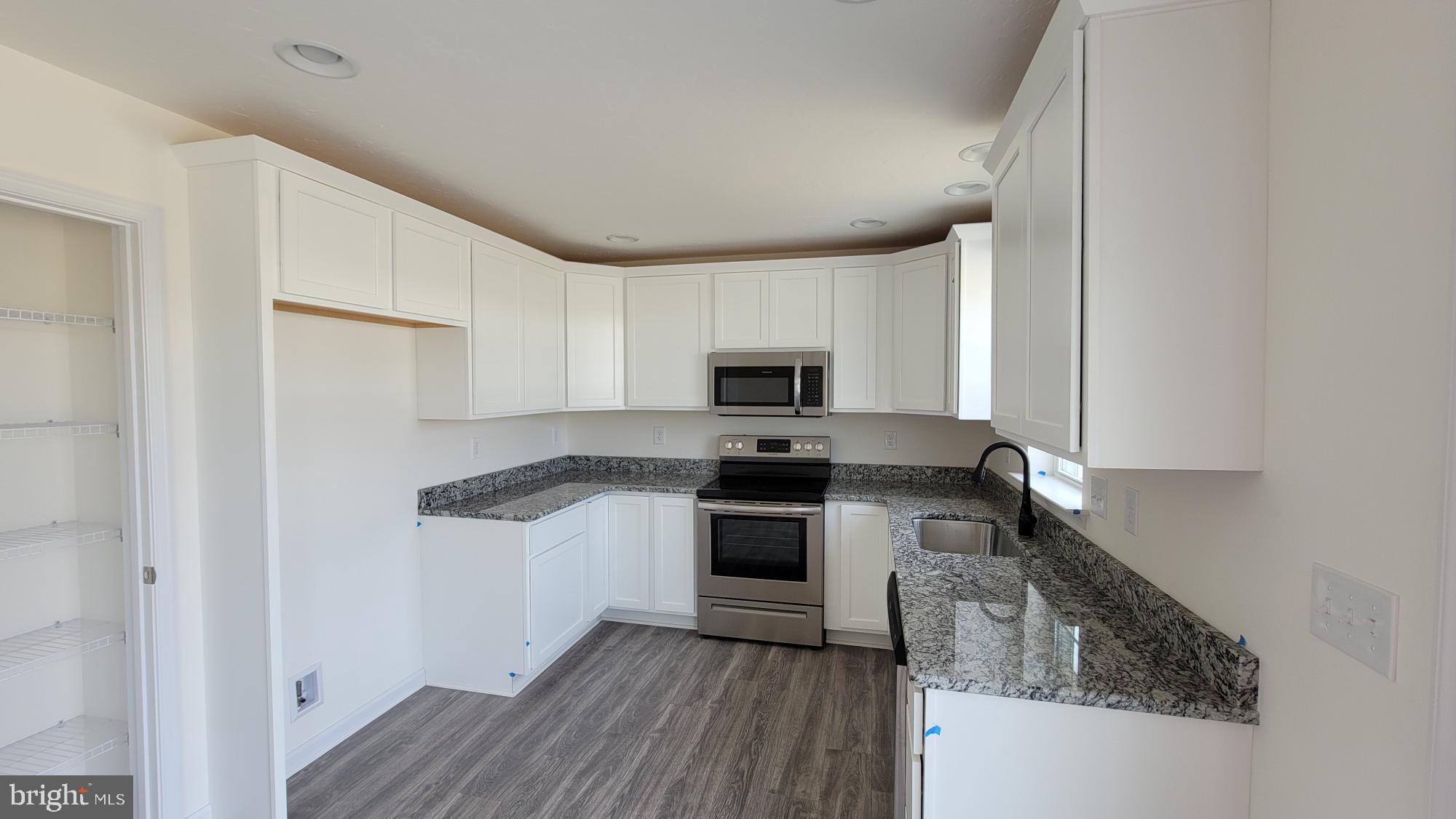 105 Piedmont Way, Unit 104 Hanover, PA 17331 - Photo 5 of 22 a kitchen with granite countertop a stove top oven a sink dishwasher and a refrigerator with wooden floor