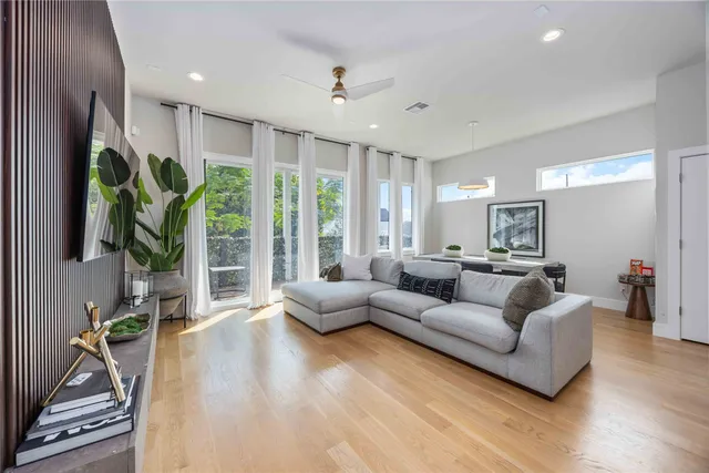 a living room with furniture potted plant floor to ceiling window and a flat screen tv