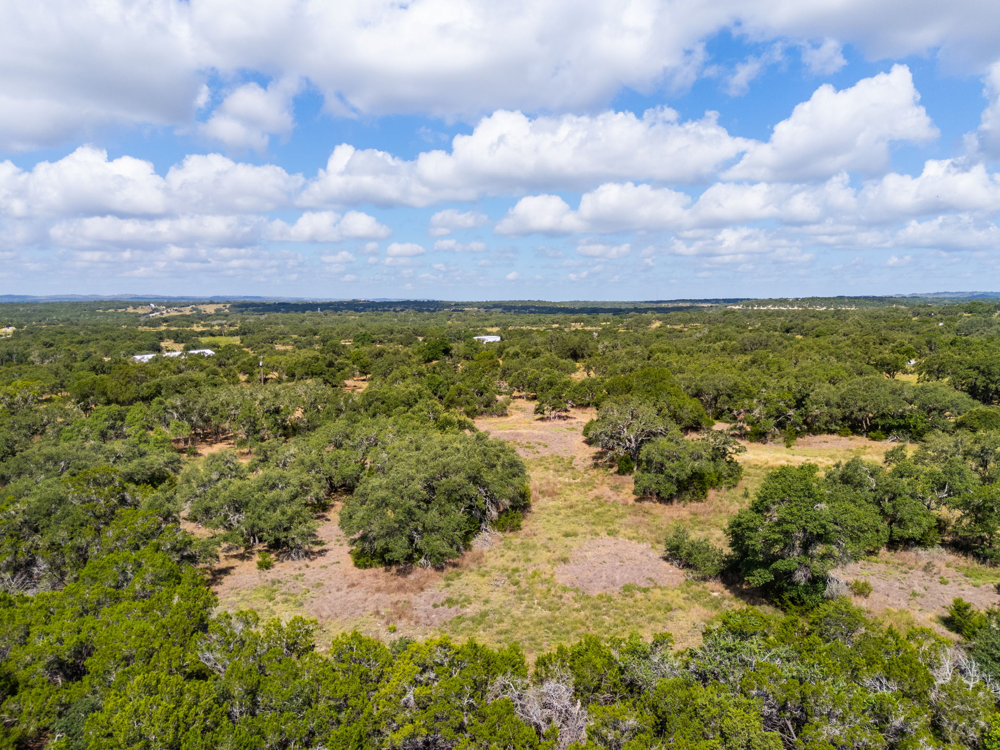 5385 Ranch Road 165 Blanco, TX 78606 - Photo 29 of 40 An aerial perspective reveals a sprawling, naturally wooded landscape under a vast blue sky with scattered clouds.