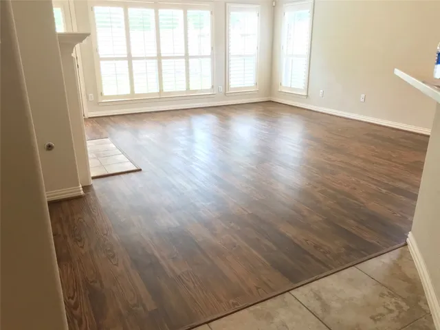 an empty room with wooden floor and windows with curtains