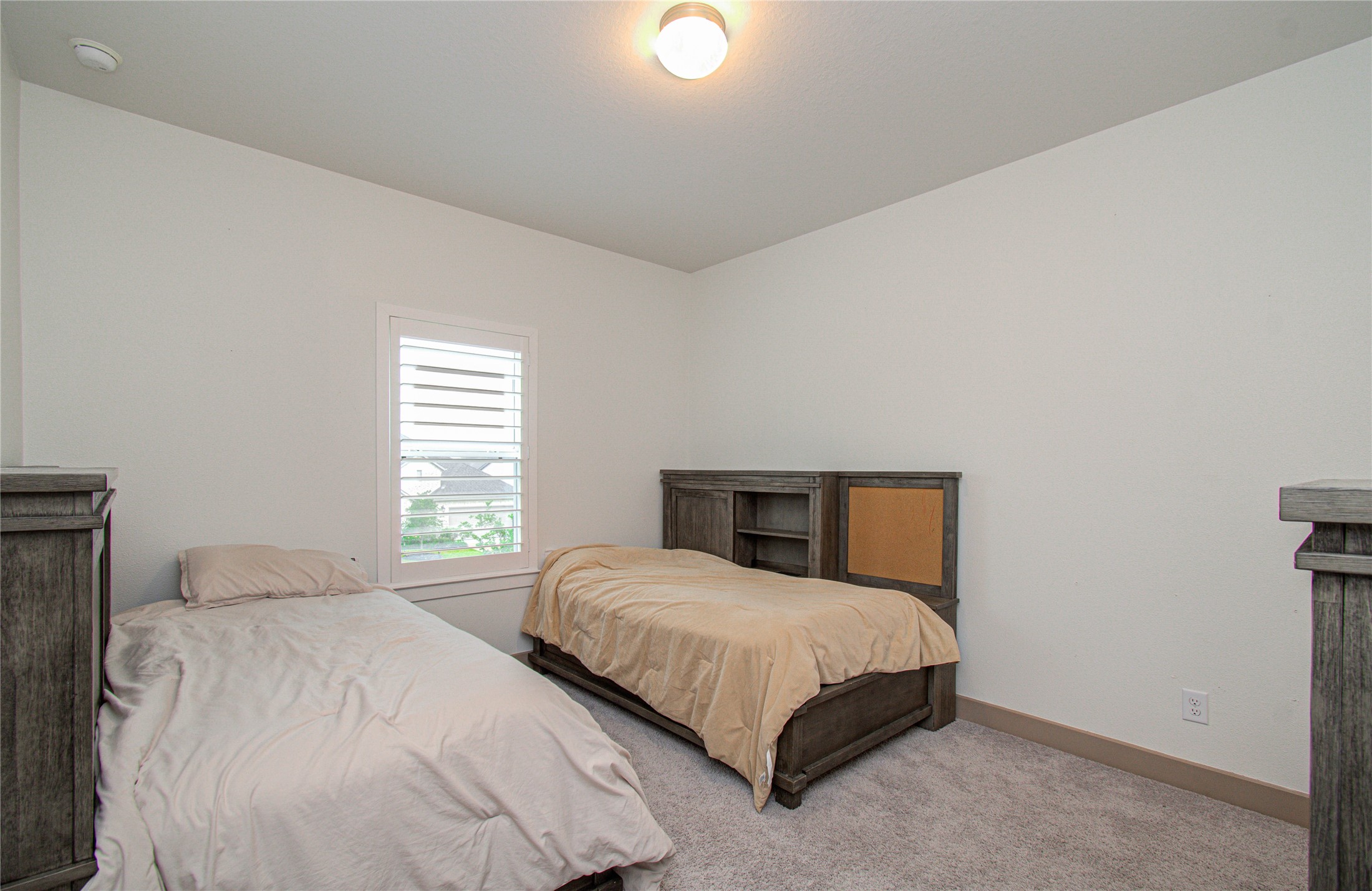 4211 Limestone Terrace Manvel, TX 77578 - Photo 24 of 33 Cozy bedroom with two twin beds, light gray carpet, and a large window with shutters for natural light. Neutral walls and simple overhead lighting create a bright, welcoming space.