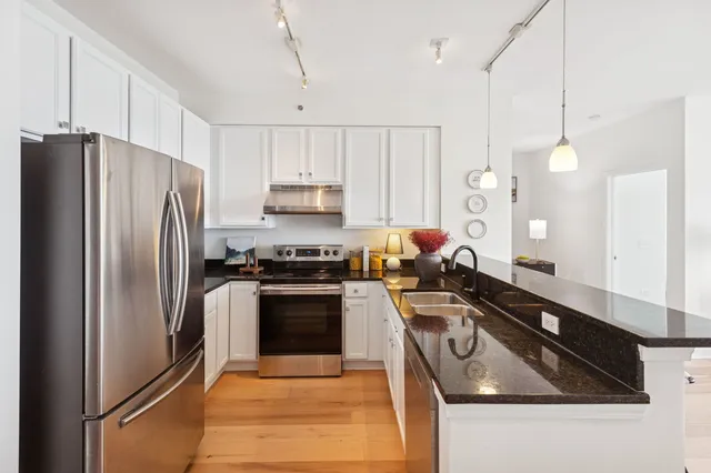 a kitchen with granite countertop a stove a sink a refrigerator and white cabinets with wooden floor