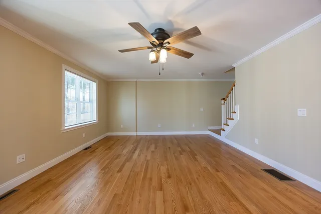 a view of an empty room with wooden floor and a ceiling fan