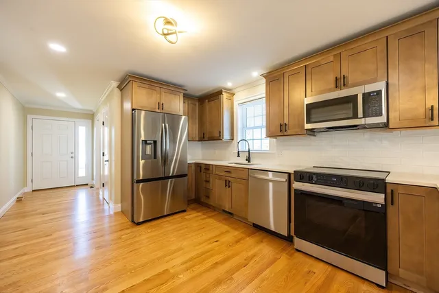 a view of an empty room and kitchen with wooden floor