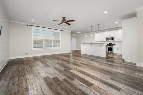 an empty room with wooden floor kitchen view and windows