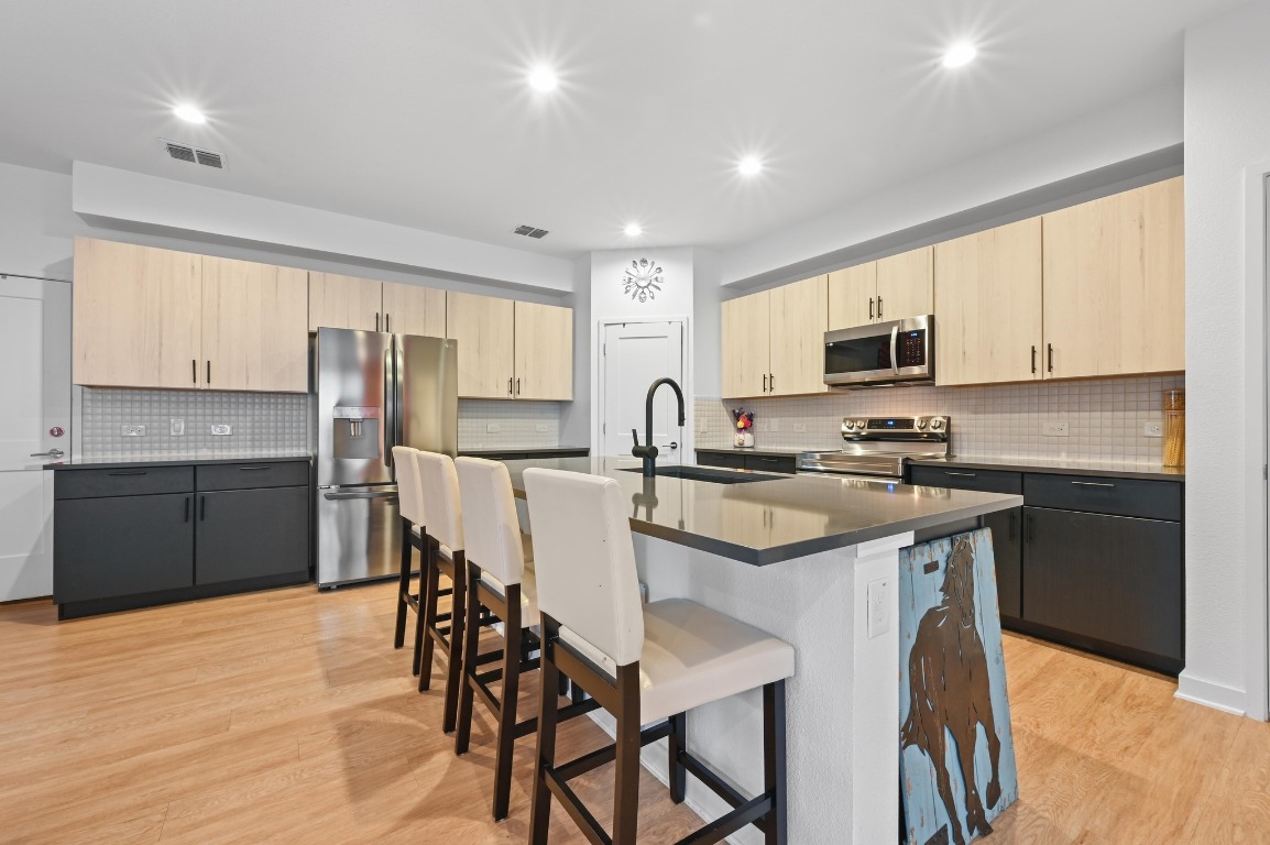 7601 Cooper Lane, Unit 6 Austin, TX 78745 - Photo 10 of 29 Kitchen featuring light brown cabinetry, stainless steel appliances, backsplash, light wood-type flooring, and recessed lighting