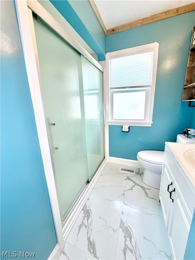 32125 Densmore Road Willowick, OH 44095 - Photo 12 of 23 Bathroom featuring a sliding frosted glass shower door, white vanity with black hardware, white toilet, and marble-look tile flooring