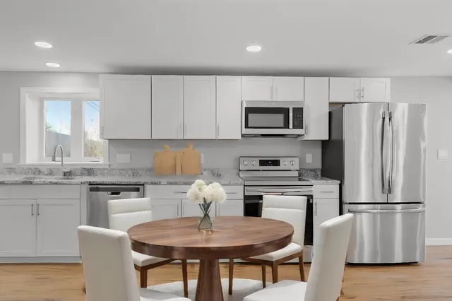 a kitchen with stainless steel appliances granite countertop a refrigerator a stove a sink a dining table and chairs