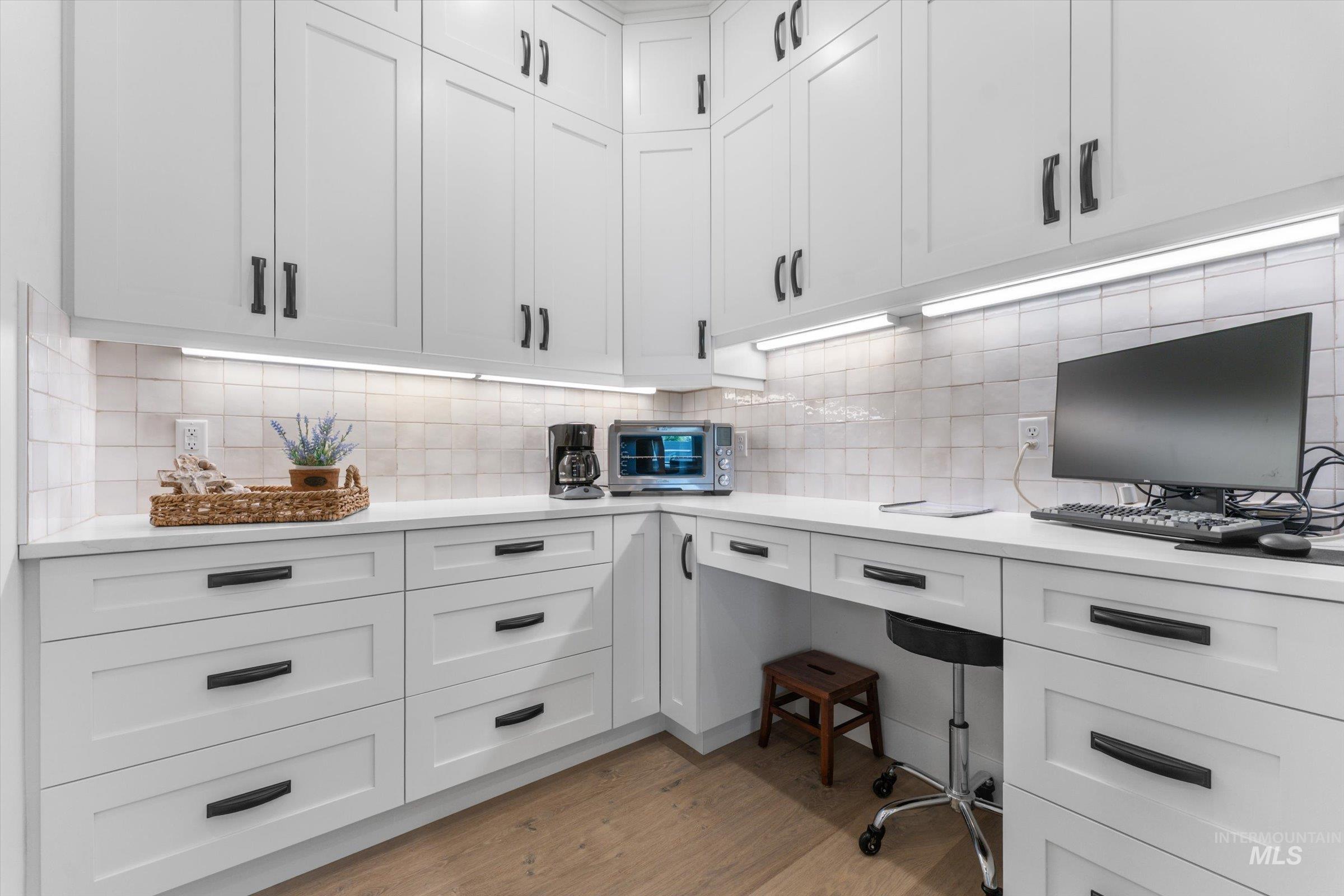 6585 South Pemberley Way Meridian, ID 83642 - Photo 16 of 43 White shaker cabinetry with dark hardware, under-cabinet lighting, light-toned tile backsplash, solid surface countertops, and wood-finish flooring