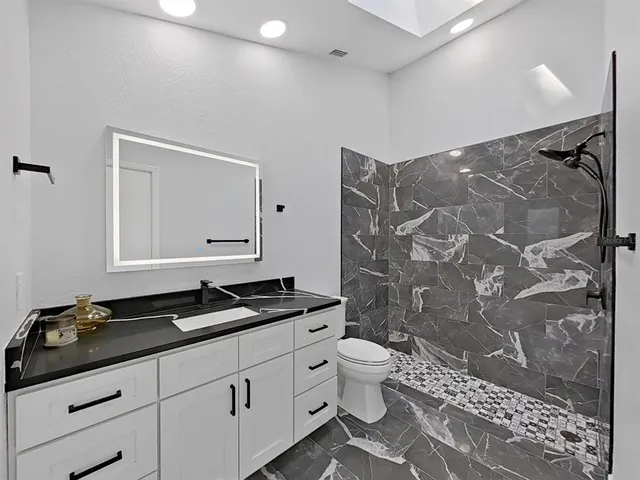 a bathroom with a granite countertop sink toilet a mirror and shower