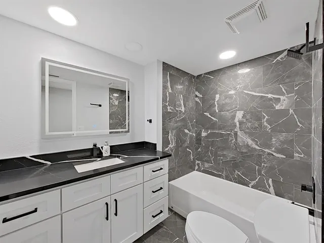 a bathroom with a granite countertop sink toilet a mirror and bathtub