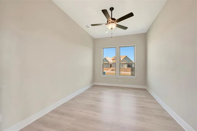 a view of an empty room with wooden floor and a ceiling fan