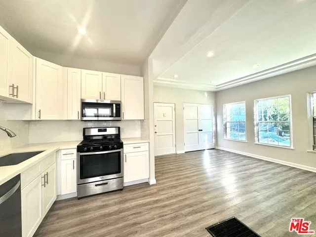 a kitchen with stainless steel appliances a stove a sink and white cabinets with wooden floor