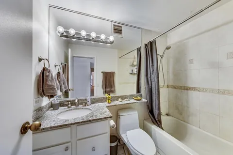 a bathroom with a granite countertop sink a toilet a mirror a bathtub and shower