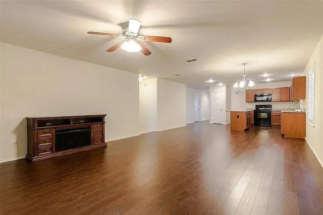 an empty room with wooden floor kitchen view and a fireplace