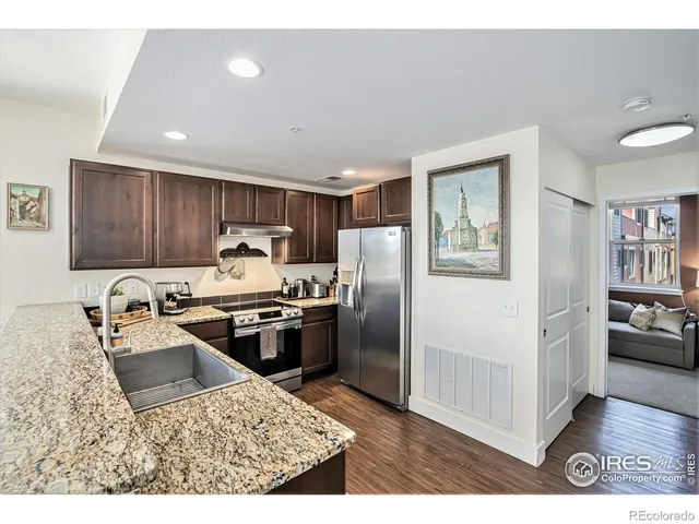 a kitchen with stainless steel appliances granite countertop a refrigerator a sink dishwasher a stove and white countertops with wooden floor