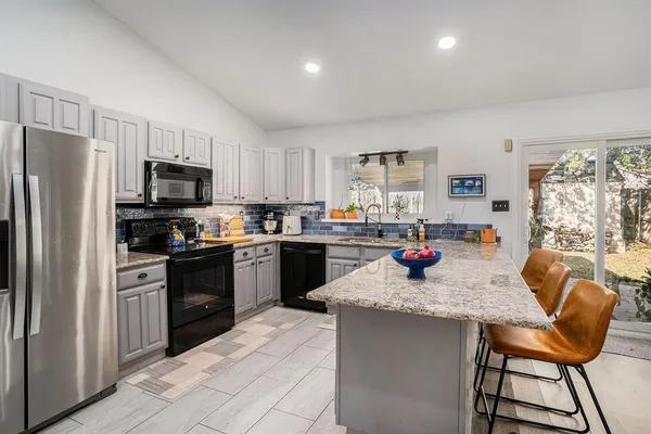 a kitchen with stainless steel appliances granite countertop a refrigerator a stove a sink dishwasher a dining table and chairs with wooden floor