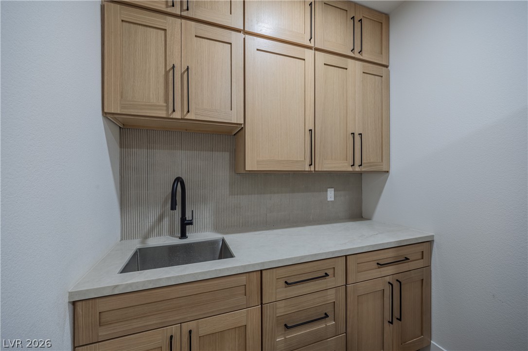 8800 Lusso Las Vegas, NV 89134 - Photo 56 of 85 Kitchen featuring tasteful backsplash, light stone countertops, light wood finish cabinetry, and a textured wall