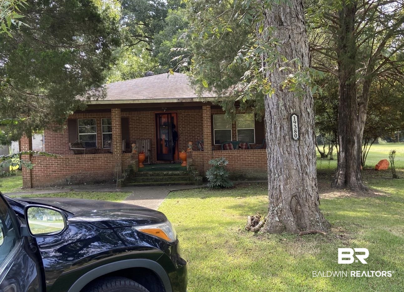 19380 Shepard Lake Road East Mount Vernon, AL 36560 - Photo 1 of 3 Brick residence featuring a covered front porch, prominent mature trees, and a visible address marker on a tree trunk
