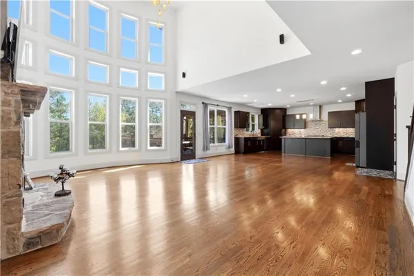 a view of an empty room with kitchen view and wooden floor
