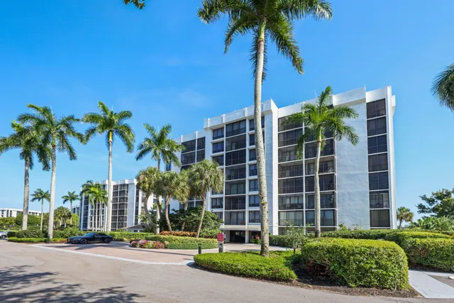 a front view of a building with palm trees and a yard