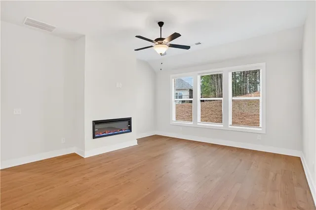 an empty room with wooden floor ceiling fan and windows