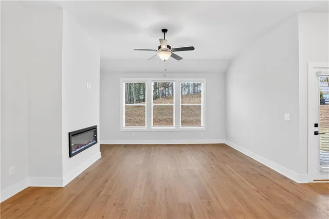 an empty room with wooden floor ceiling fan and windows