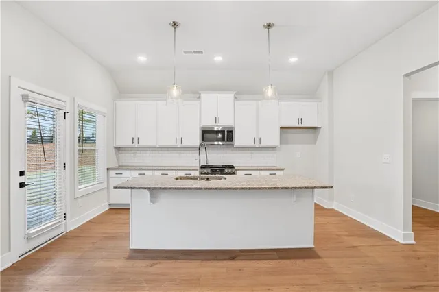 a large kitchen with stainless steel appliances granite countertop a stove a sink dishwasher a refrigerator and white cabinets with wooden floor