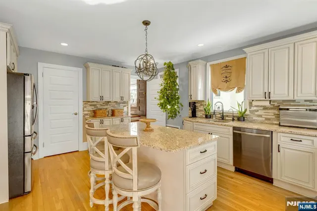 a kitchen with stainless steel appliances granite countertop a stove a refrigerator and white cabinets with wooden floor