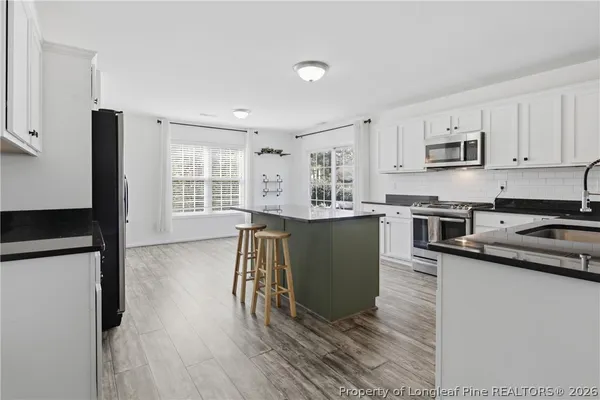 a kitchen with stainless steel appliances kitchen island granite countertop a refrigerator a stove top oven a sink dishwasher and white cabinets with wooden floor