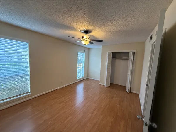 an empty room with wooden floor chandelier fan and windows