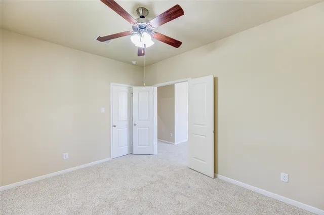 an empty room with a chandelier fan and windows