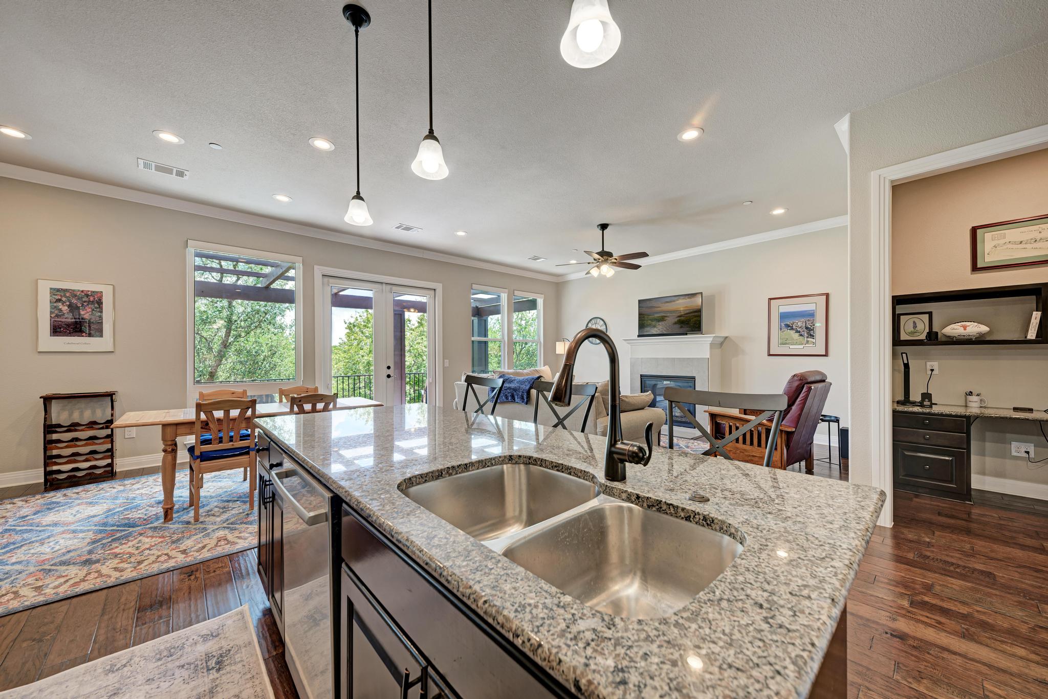 2601 North Quinlan Park Road, Unit 506 Austin, TX 78732 - Photo 17 of 39 A gourmet kitchen island with granite counters flows into a bright, open living area, featuring a fireplace and balcony access.