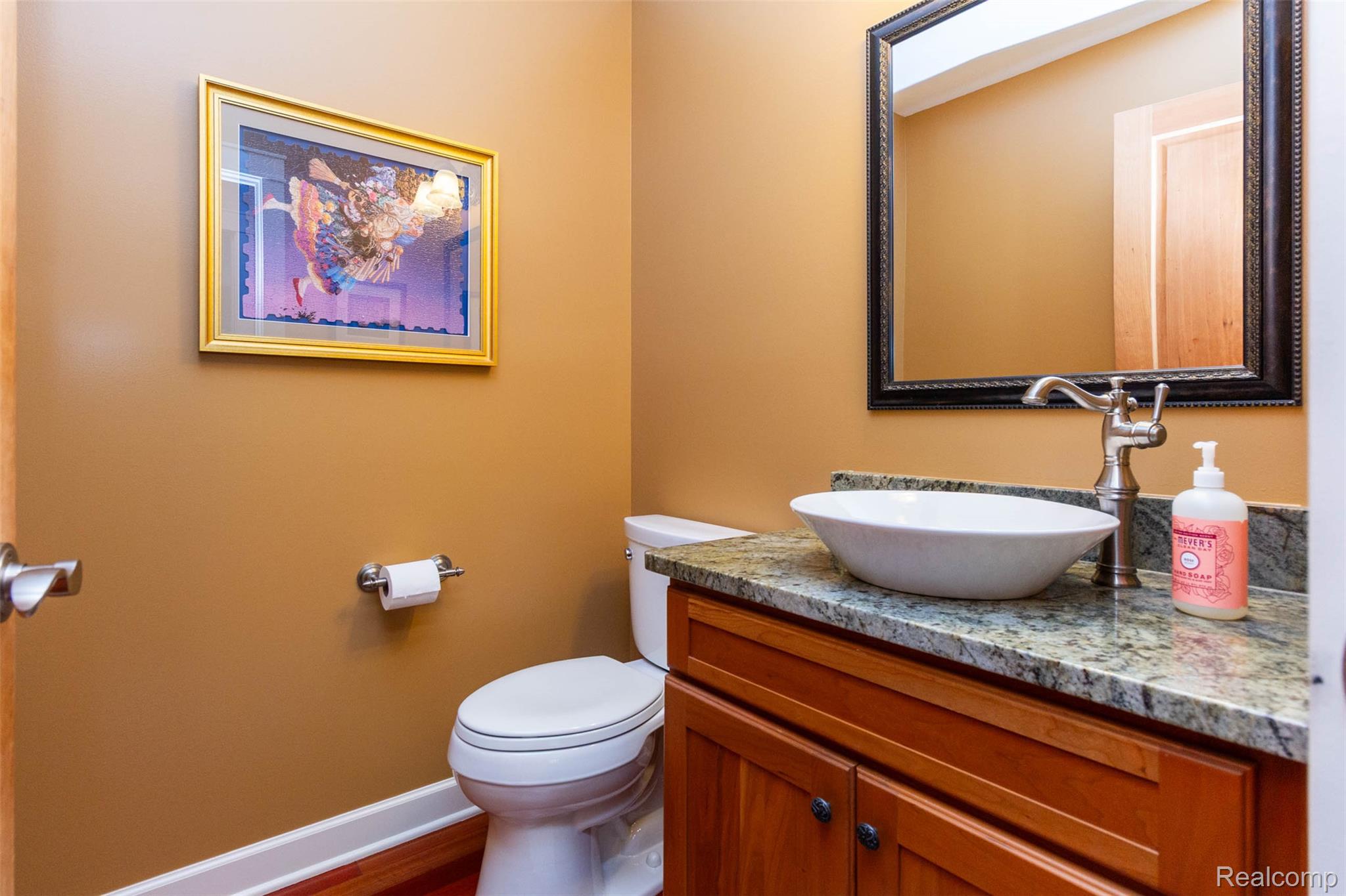 9887 Hadley Road Clarkston, MI 48348 - Photo 26 of 56 Powder room featuring a vessel sink, stone countertop, wood-finish vanity, and a framed mirror