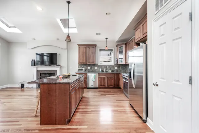 a kitchen with stainless steel appliances granite countertop a stove top oven a sink dishwasher a refrigerator and a dining table with wooden floor