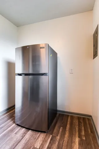 a view of a refrigerator in kitchen and an empty room with wooden floor